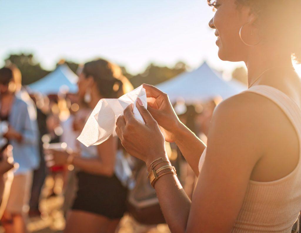An image of a woman at a festival wiping her hands on a wet wipe.