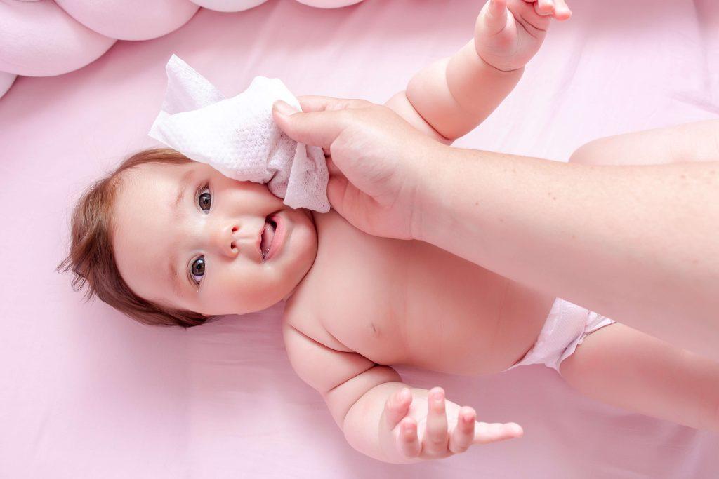 A baby being wiped with a sensitive wet wipe, laying in a pink crib.